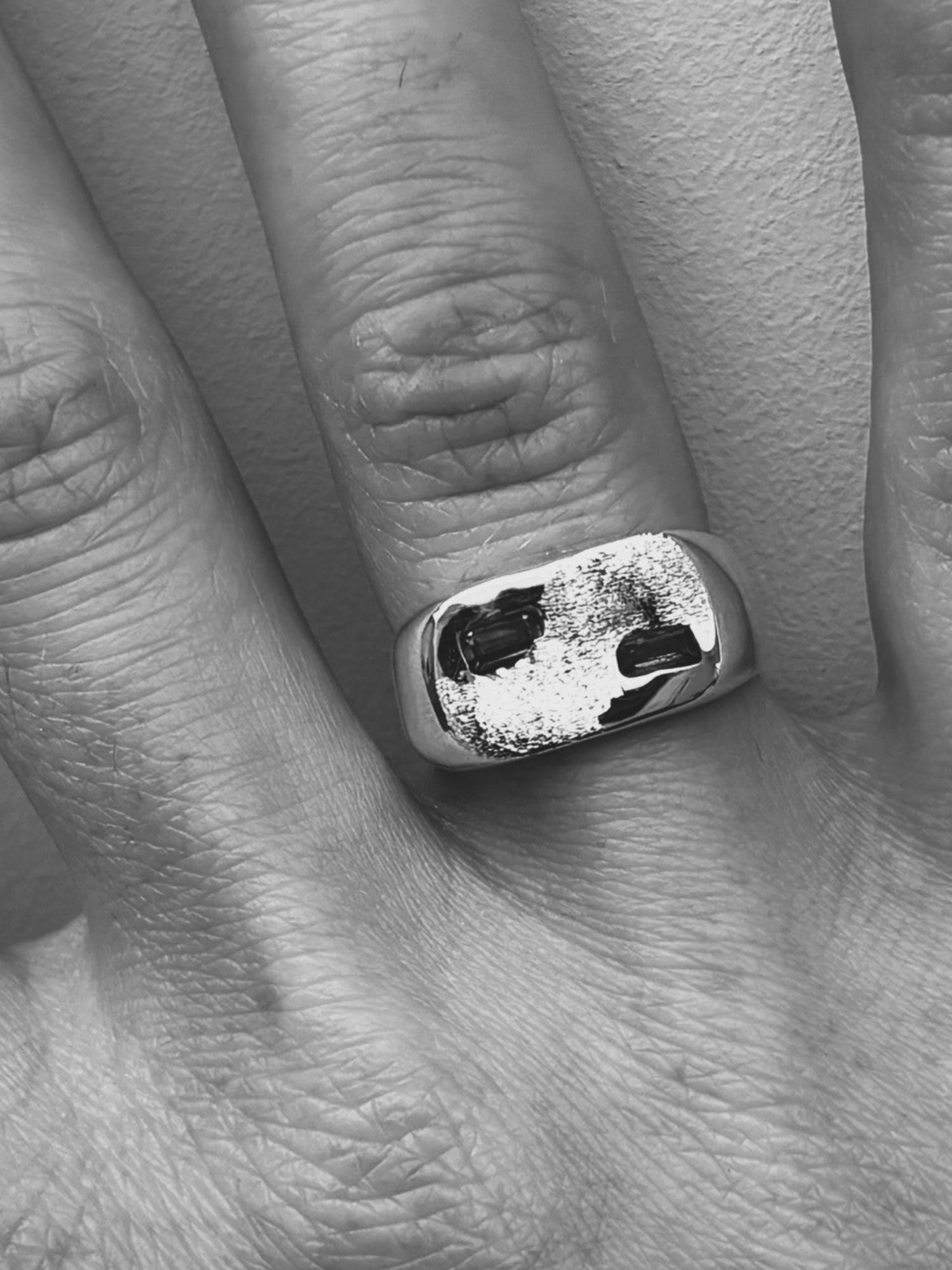 Black and white photo of a hand with a ring on a plain background